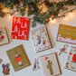 Collection of Christmas-themed cards on a white surface with decorative lights and greenery.
