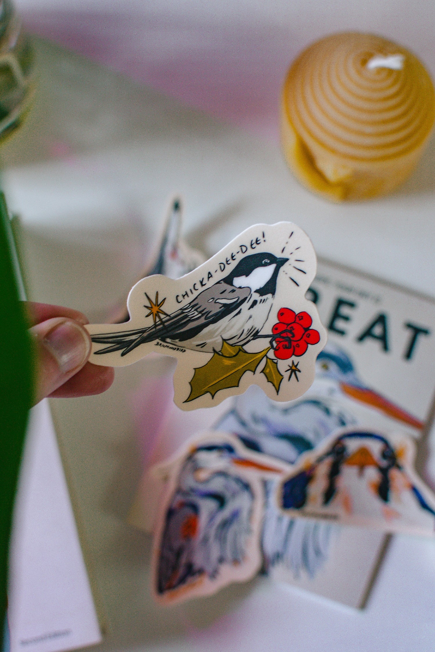 Hand holding a chickadee sticker on a blurred background