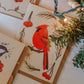 Set of greeting cards with cardinal and bird illustrations on a white surface with greenery.