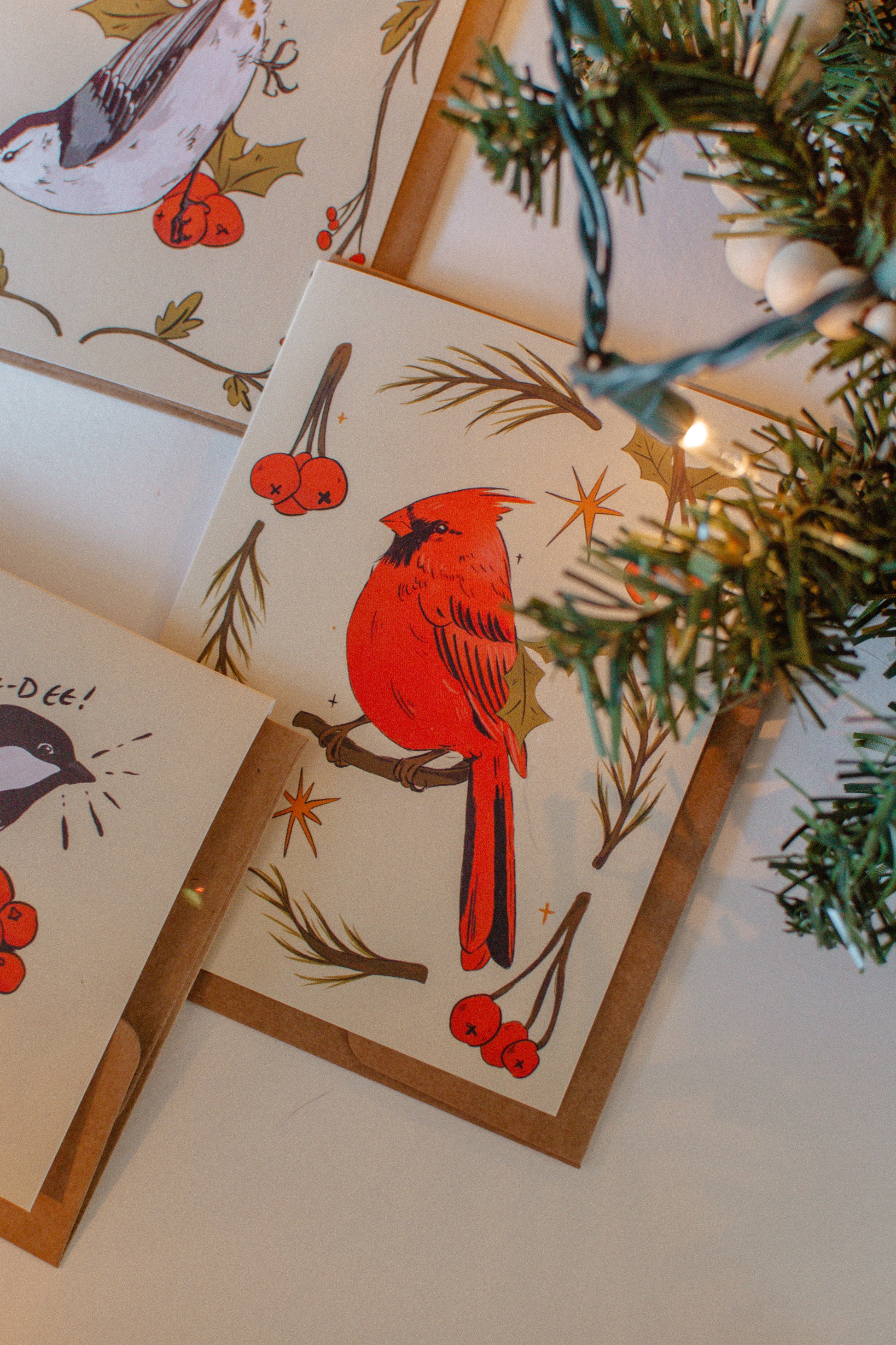 Set of greeting cards with cardinal and bird illustrations on a white surface with greenery.