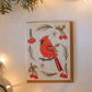 Greeting card of a red cardinal bird with berries on a white background, surrounded by Christmas lights and greenery.