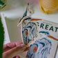 Hand holding a Great Blue Heron Sticker with a matching card design in the background