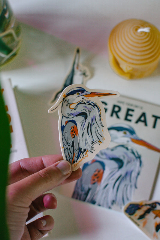 Hand holding a Great Blue Heron Sticker with a matching card design in the background