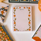Notepad with floral design and decorative cards on a white surface