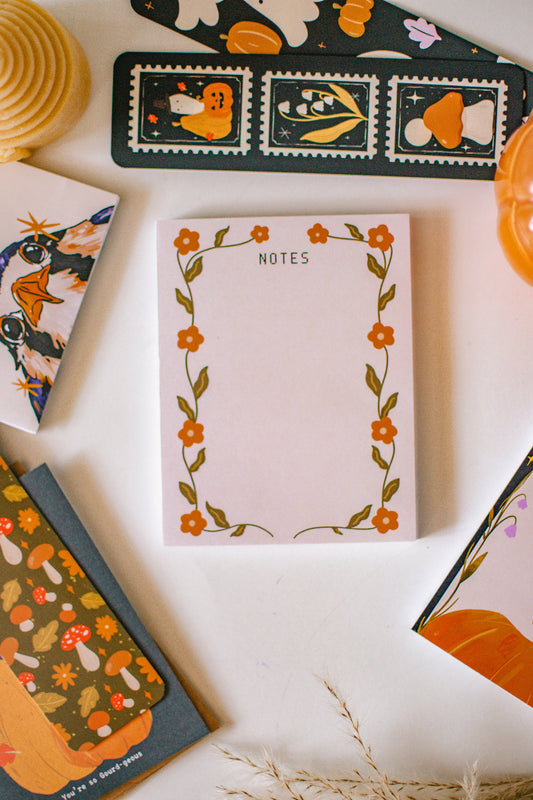 Notepad with floral design and decorative cards on a white surface